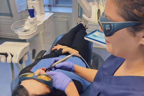 Tandlæge udfører laserbehandling på patient i moderne tandlægeklinik - tandlægen bærer beskyttelsesbriller og arbejder med laserprocedure