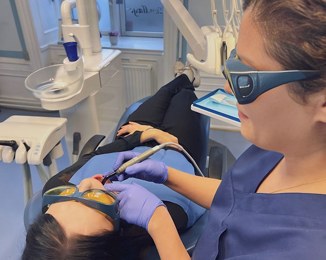 Tandlæge udfører laserbehandling på patient i moderne tandlægeklinik - tandlægen bærer beskyttelsesbriller og arbejder med laserprocedure